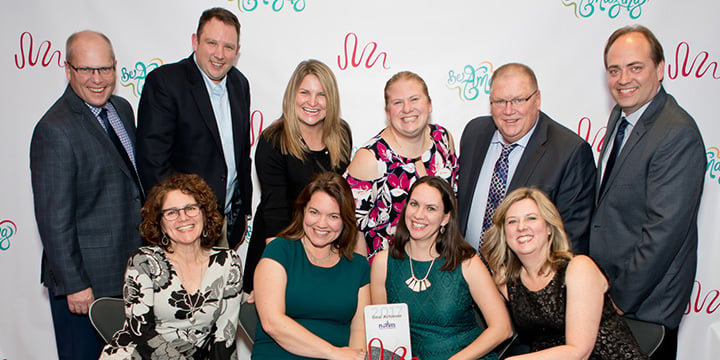 A group of ten people smiling at the camera, holding a plaque that reads "2017" 