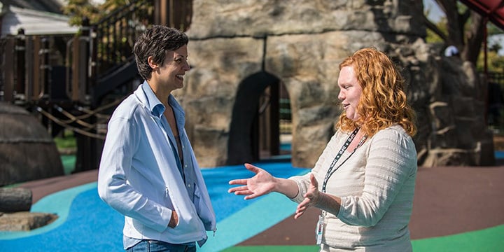 Two women talking, one gesturing with her hands while the other laughs. 