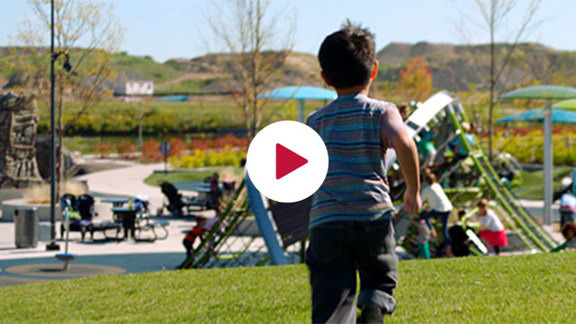 Boy running away from camera to a playground with a Crab Trap climber. A white circle sits in the center of the image with a red triangle looking like a play button.