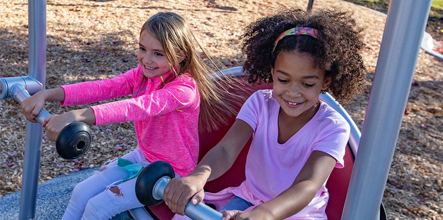 Two girls sitting on one side of the We-Go-Swing, inclusive playground swing set