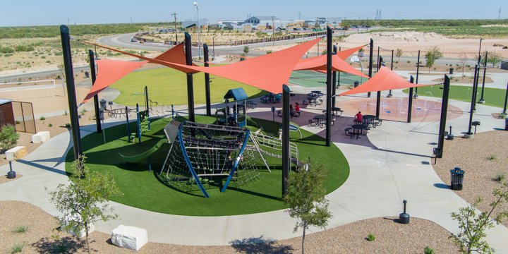 Outdoor play structure with Crab Trap net-based climber in the foreground covered with rust-colored shade sails. 