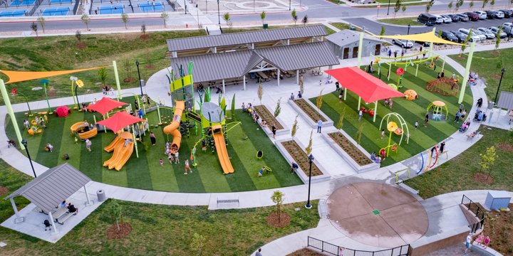 Huge outdoor playground with multple orange and red play features including a tall climbing tower with twisty slide and double slide, other playstructures with slides, freestanding inclusive spinners and swings. 