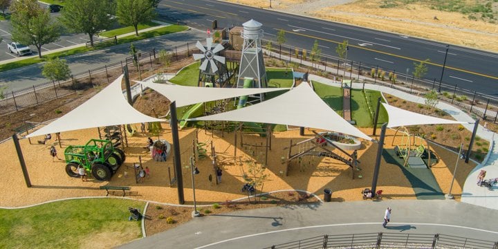 Farm and countryside themed playground with a custom silo play structure and windmill play structure in the background and a green custom tractor climber in the foreground. 