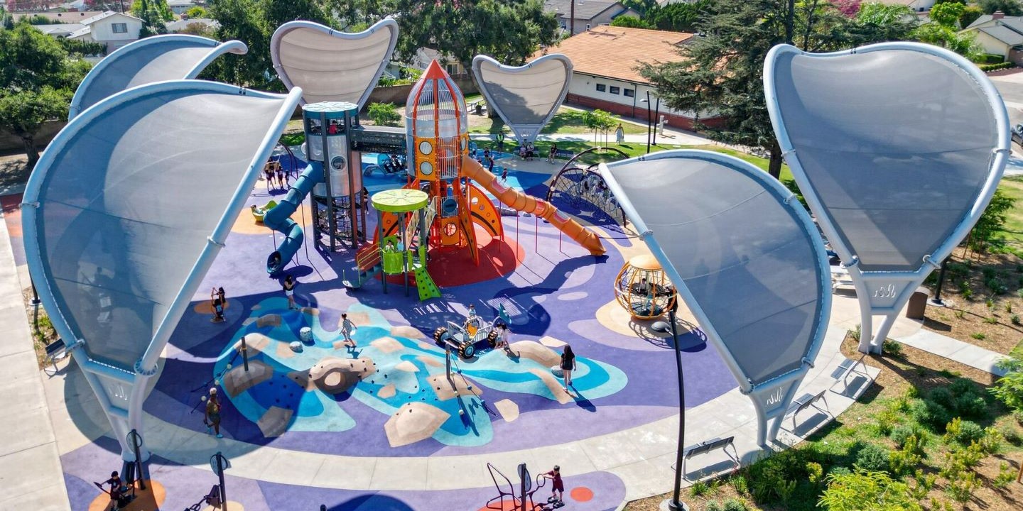 Overhead view of colorful playground with orange rocket-themed climber and arching custom shade structures that curve over the playground from its periphery.