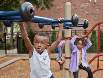 Closeup on boy playing on overhead monkey bars with little girl in background