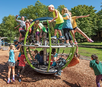 Numerous children playing on a cable net spinning playground structure