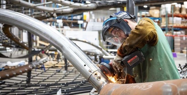 A Landscape Structures employee working in the shop on a playground component, showing sparks flying from where he is working on the metal feature.