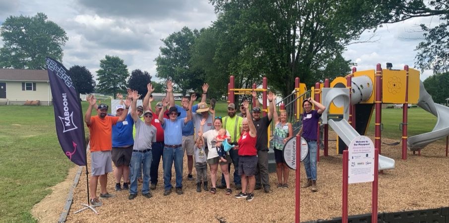 A group of people on a playground are lined up together, and raise their hands in the air