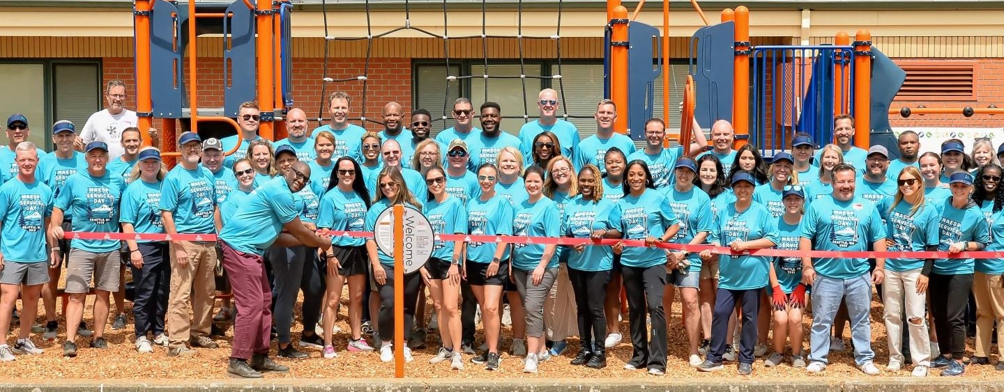 A large group of people in matching blue t-shirts stand in front of a playground structure