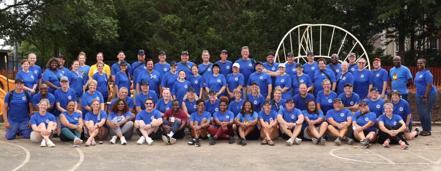 A group photo of many adults in blue tshirts standing in front of a playground climber