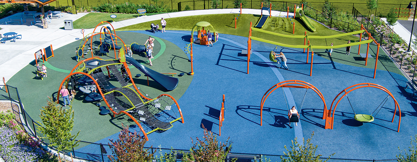 Overhead view of a playground with bright blue surfacing and green grass around the edges