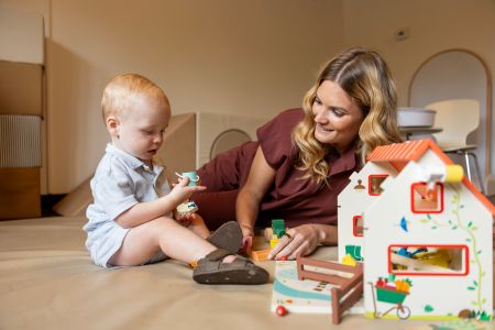 A woman lies on her side watching a toddler hold and look intently at an object