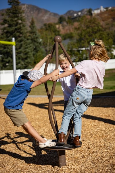 Three children ride on a playground spinner