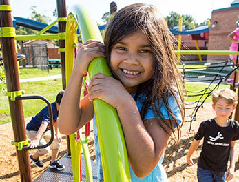 A young girl shown climbing a bright lime green Spiderweb Climber on a school playground.