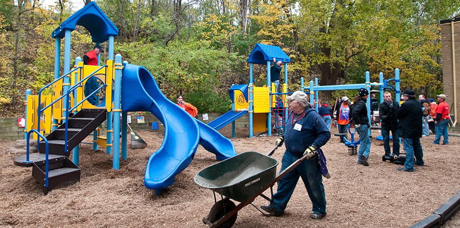 KABOOM! volunteer pushing an empty wheelbarrow at a playground build site.