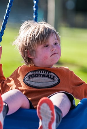 A little boy sits on a blue swing. 