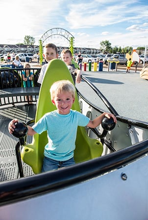 A little boy smiles into the camera while sitting on a lime green seat on a playground structure. 